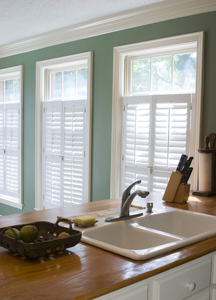 A green kitchen featuring white shutters. 