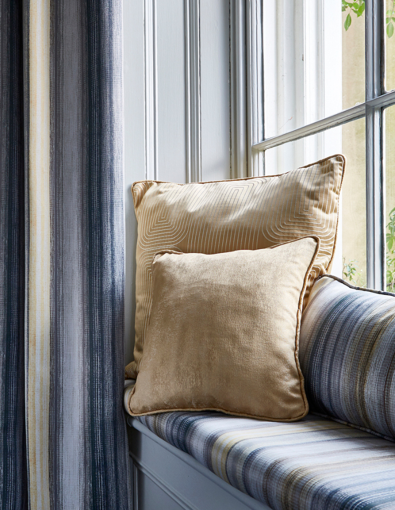 A coastal chic window seat with blue curtains and sand coloured cushions. 