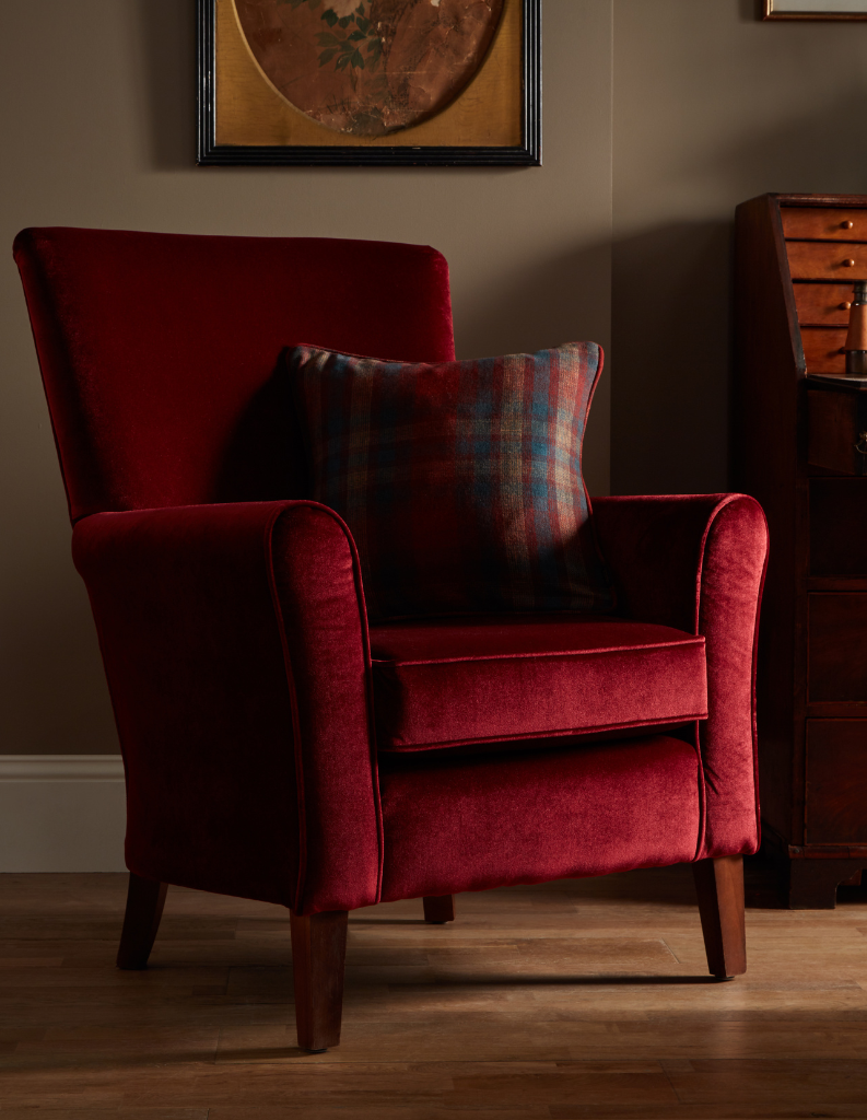 A deep wine red arm chair with tartan cushion.