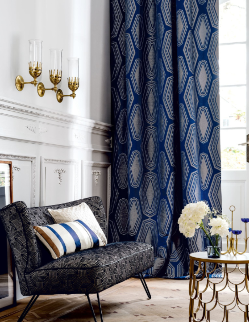 An eclectic living room featuring bold blue curtains, stripy cushions and white walls.