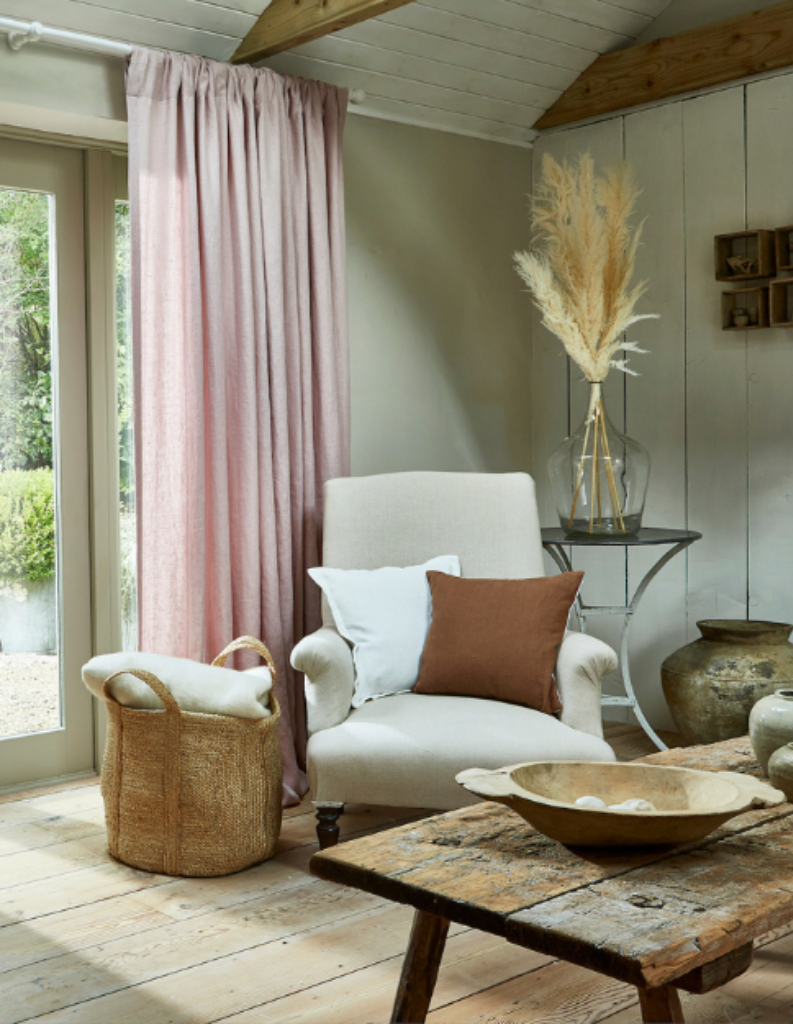 A bright country space with a light pink curtain alongside wooden beams and furniture.