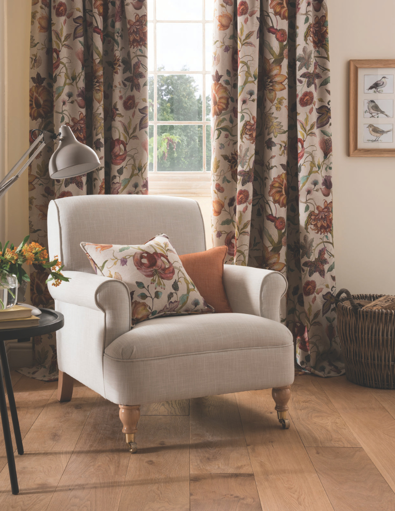 An autumn inspired living room with floral curtains, orange cushions and a comfy grey chair. 