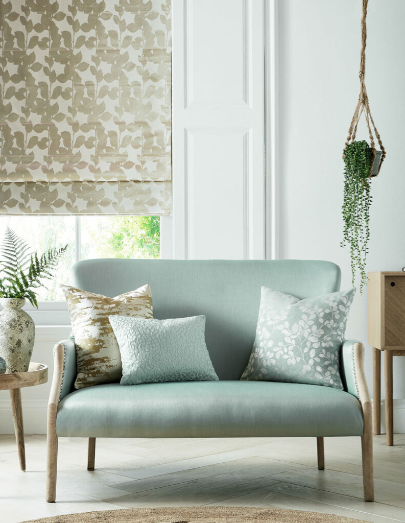 A chic living room featuring a golden Roman blind, mint green sofa and plants. 