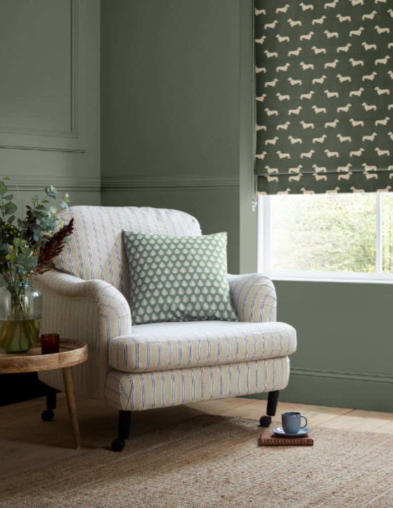 A living room featuring forest green Roman blinds and a forest green cushion on the chair.