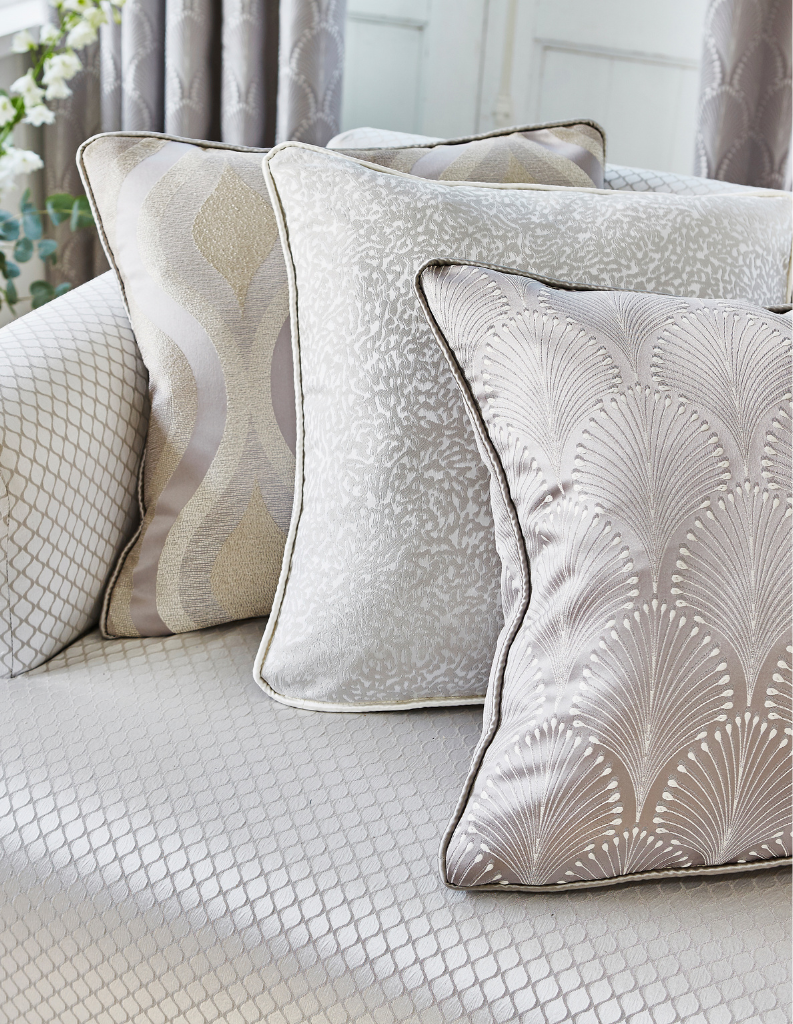 Scallop patterned cushions on a silver sofa with patterned curtains behind. 