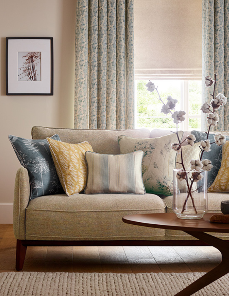 A cosy living room with patterned cushions and a layered window with Roman blind and curtains.